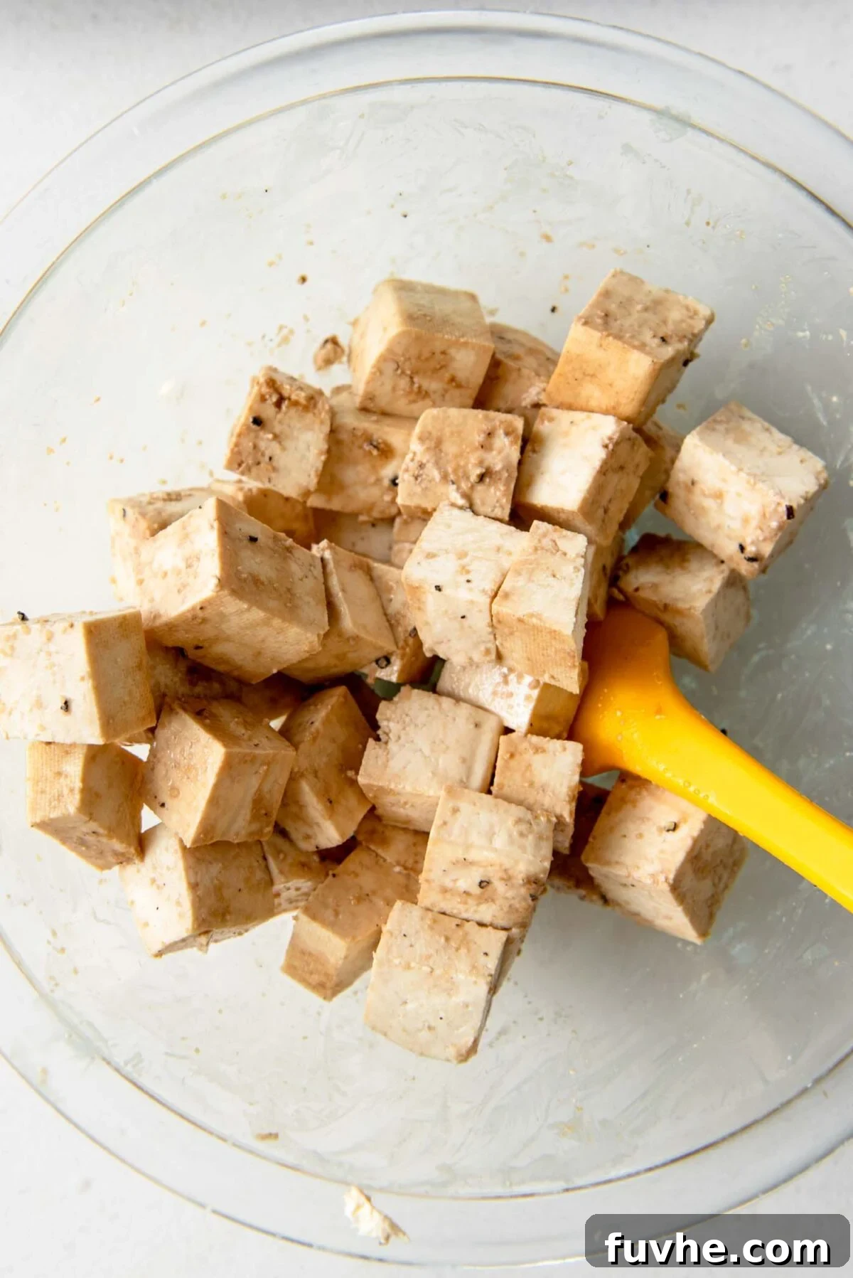 Tofu cubes coated in soy sauce, cornstarch, and spices in a mixing bowl, ready for baking.