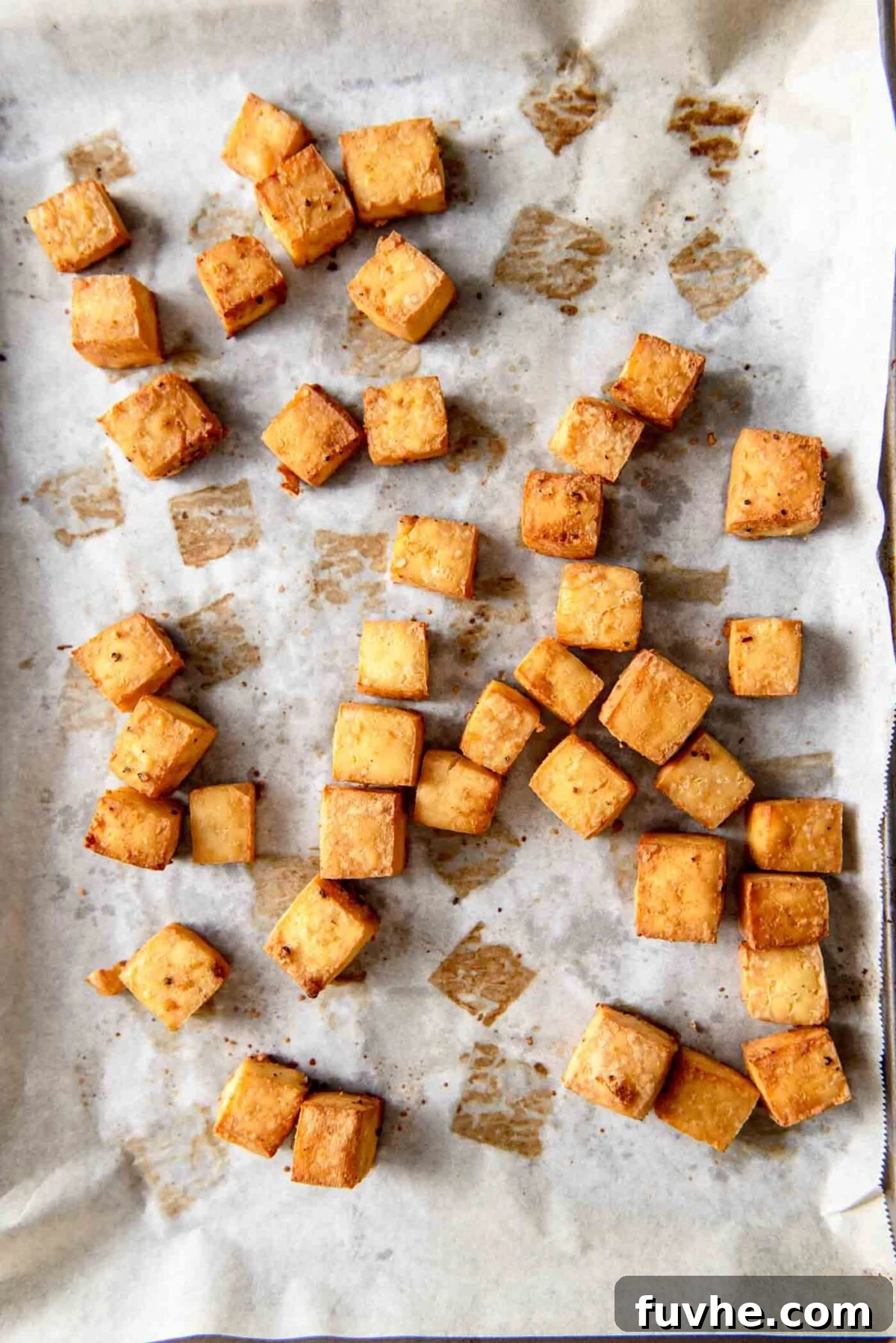 Golden brown, crispy baked tofu cubes spread evenly on a parchment-lined baking sheet, fresh out of the oven.