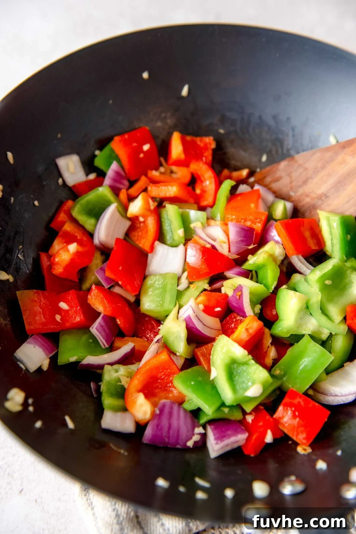 Vibrant chopped bell peppers and red onion stir-frying in a wok alongside the fragrant garlic and ginger.