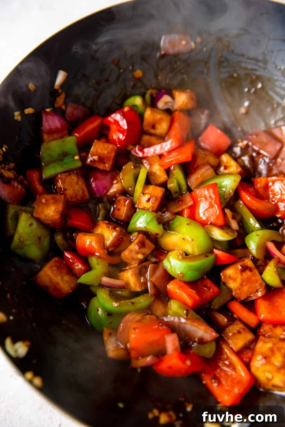 Crispy tofu cubes, colorful bell peppers, and sliced onions coated in a rich, glossy Kung Pao sauce, simmering together in a wok.