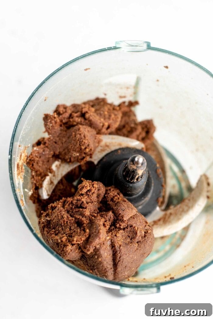 Raw chocolate energy ball dough being blended in a food processor, forming a cohesive ball.