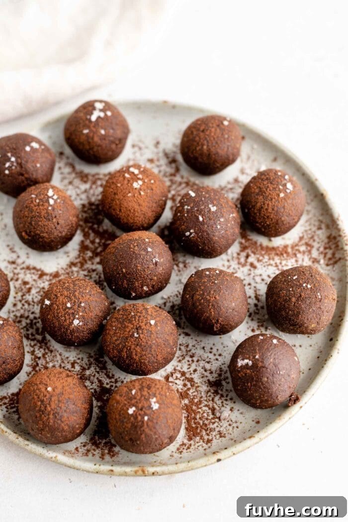 A plate of perfectly rolled raw chocolate energy balls, some sprinkled with chocolate shavings.