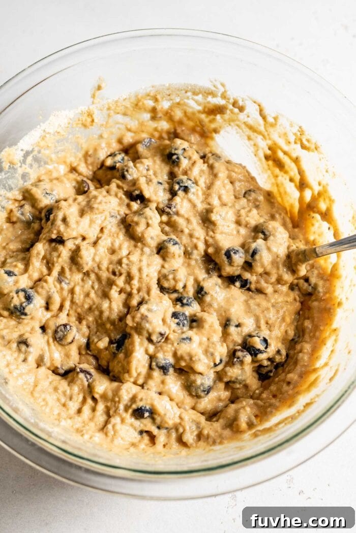 Raw muffin batter in a mixing bowl with blueberries and chocolate chips in it.