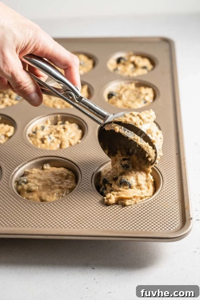 Scooping muffin batter into a muffin tin using an ice cream scoop.