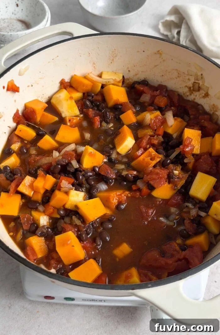 Hearty Butternut Squash Black Bean Chili 6 Cubed butternut squash, black beans, and diced tomatoes simmering gently in a rich, tomato-based broth in a large soup pot.