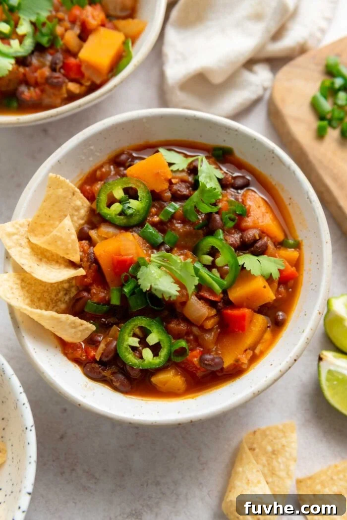 Hearty Butternut Squash Black Bean Chili 8 A beautifully presented bowl of butternut squash chili, adorned with fresh jalapeno, vibrant green onion, aromatic cilantro, and crunchy tortilla chips, ready for enjoyment.