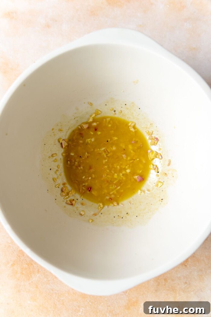 A glistening shallot Dijon salad dressing, freshly whisked and ready in a large mixing bowl, awaiting the addition of fresh ingredients.