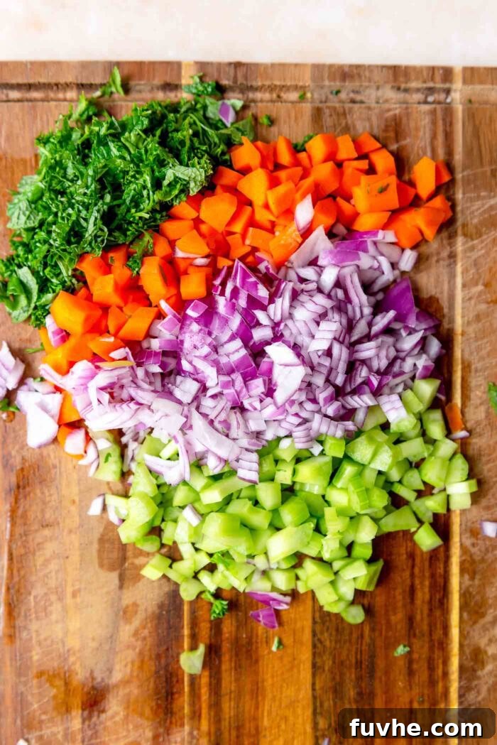 A colorful array of chopped fresh herbs, red onion, carrot, and celery neatly arranged on a wooden cutting board, prepped for the salad.