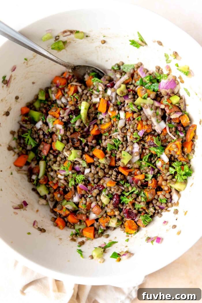 A bountiful French lentil salad, rich with colorful vegetables and herbs, beautifully mixed in a large serving bowl, showcasing its readiness to be enjoyed.