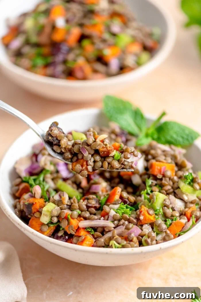 A forkful of vibrant French lentil and fresh herb salad gracefully held above a bowl brimming with the same delicious salad, inviting a taste.