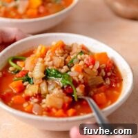 Spoon in a bowl of vegetable barley soup with sweet potato and spinach.