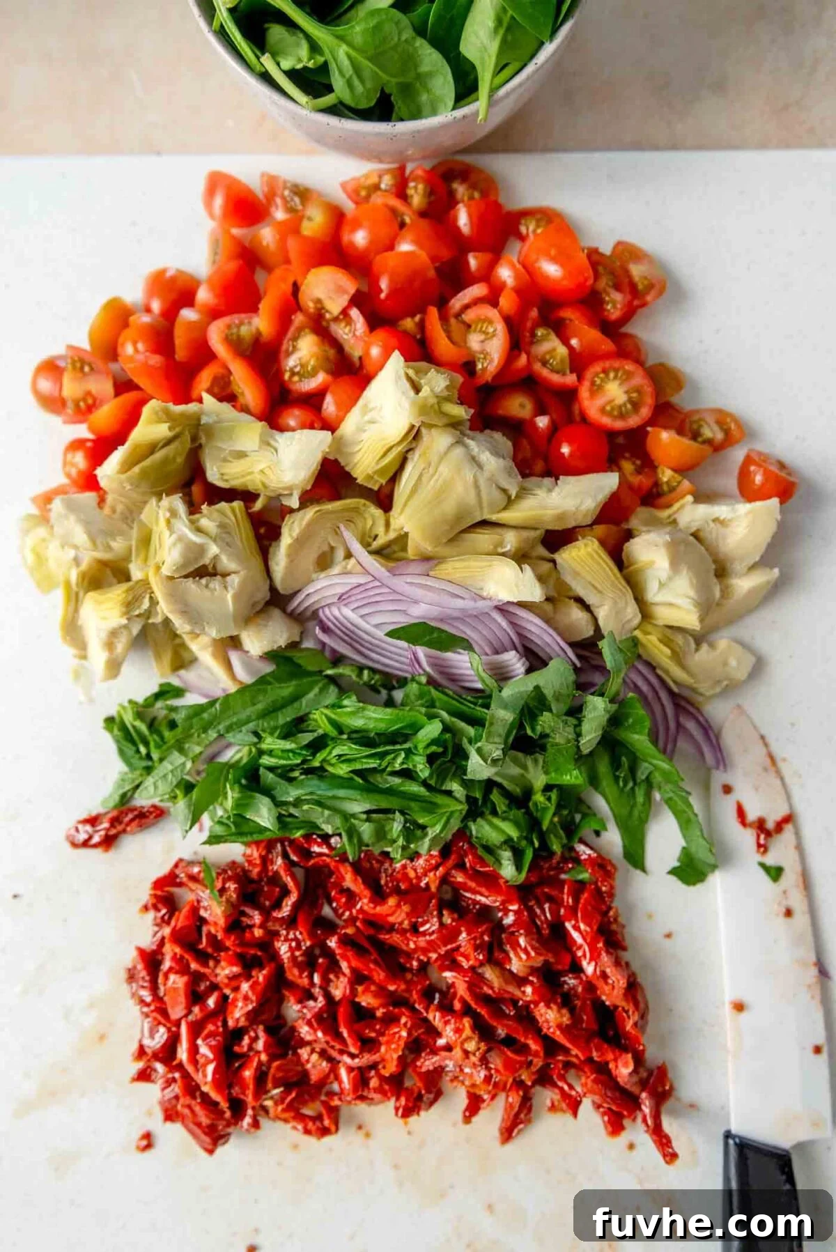 Tuscan Sun-Dried Tomato Pasta Salad 5 Chopped grape tomatoes, artichoke hearts, basil, red onion and sun dried tomatoes on a cutting board.