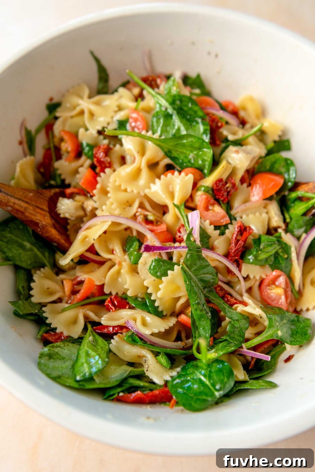 Tuscan Sun-Dried Tomato Pasta Salad 6 Sun dried tomato pasta salad with fresh spinach, red onion, cherry tomatoes and artichokes in a mixing bowl.