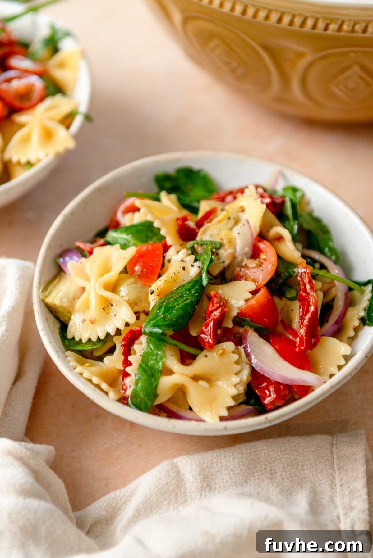 Tuscan Sun-Dried Tomato Pasta Salad 7 Bowl of sun dried tomato pasta salad with spinach, red onion and artichokes.