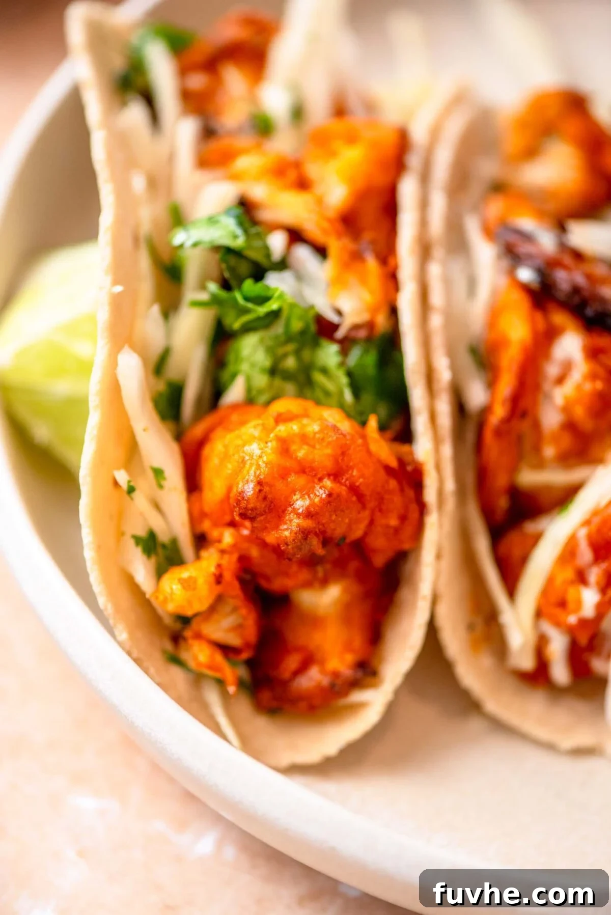 Crispy Buffalo Cauliflower Tacos 10 A plate of two perfectly assembled buffalo cauliflower tacos, garnished with cilantro and cabbage slaw.