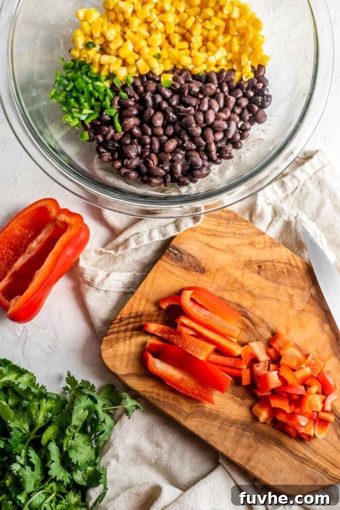 Fiesta Black Bean and Corn Salad 4 Finely chopped red bell pepper on a wooden cutting board, with a bowl nearby containing black beans, corn, and minced jalapeño, showcasing the fresh ingredients for the salad.