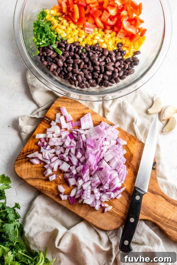 Fiesta Black Bean and Corn Salad 5 Diced red onion on a wooden cutting board, positioned next to a mixing bowl filled with black beans, corn, and bell pepper, illustrating the preparation process.