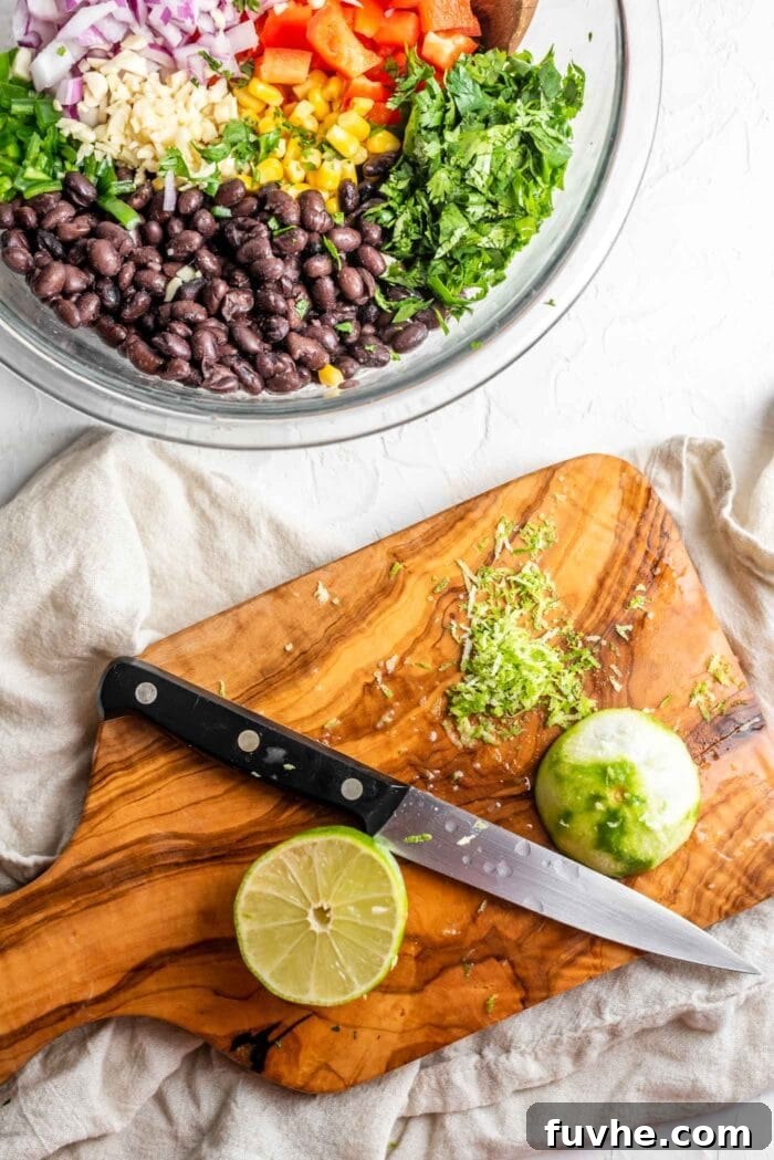 Fiesta Black Bean and Corn Salad 6 A close-up shot of a knife finely chopping fresh lime zest on a wooden cutting board, with a blurred background of a bowl containing black bean corn salad ingredients, highlighting the zest preparation step.