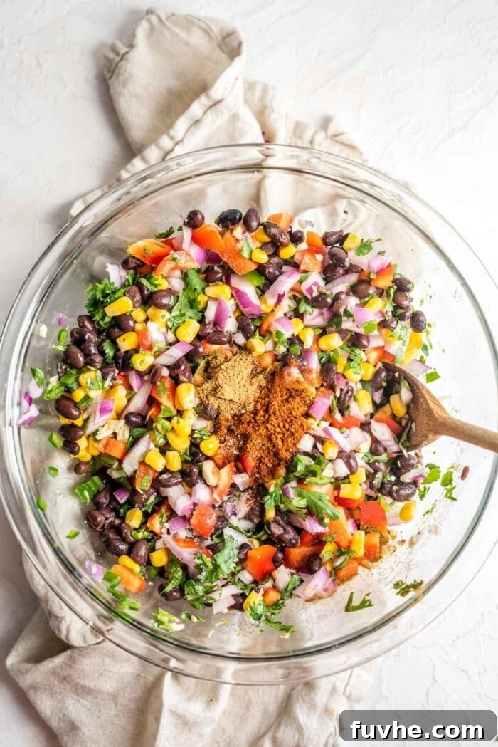 Fiesta Black Bean and Corn Salad 8 A glass mixing bowl with Southwest black bean corn salad, clearly showing the vibrant red onion and bell pepper mixed throughout the beans and corn, demonstrating the fully combined ingredients.
