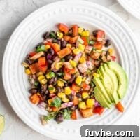 Black bean corn salad with avocado on a small white plate with cilantro and lime on the side.