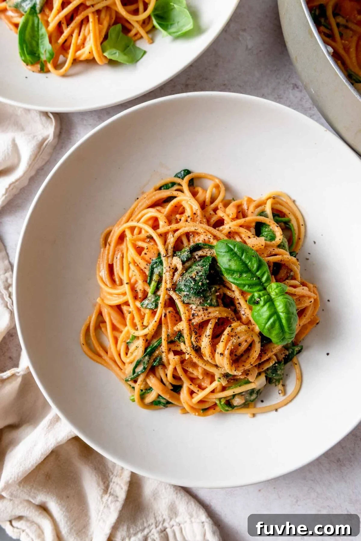 Bowl of creamy tomato pasta topped with a few leaves of fresh basil and fresh cracked black pepper.