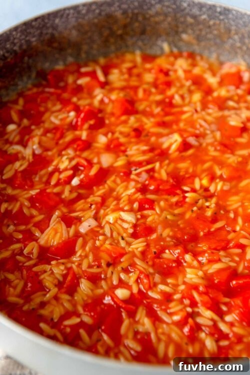 Orzo cooking in a tomato sauce in a large pan.