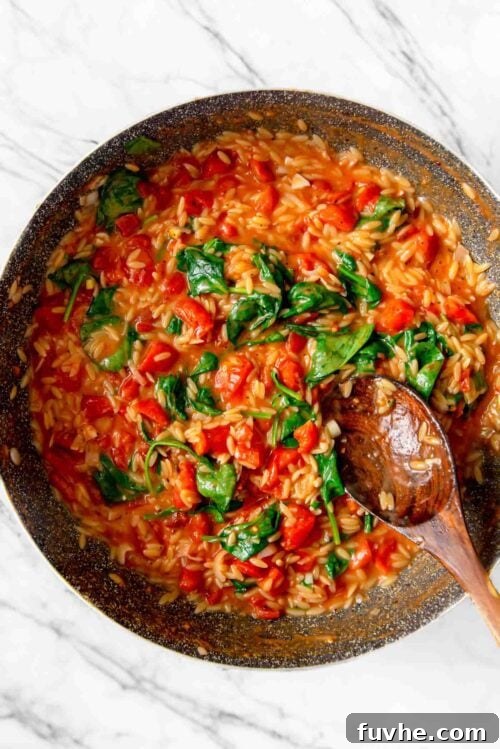 Large pan of tomato orzo with spinach with a wooden spoon resting in pan.