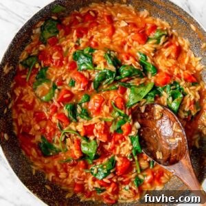 Large pan of tomato orzo with spinach with a wooden spoon resting in pan.