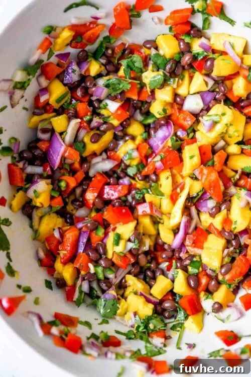 All the vibrant ingredients of the mango black bean salad, including diced mango, black beans, red bell pepper, red onion, and cilantro, tossed together in a large mixing bowl with the dressing.