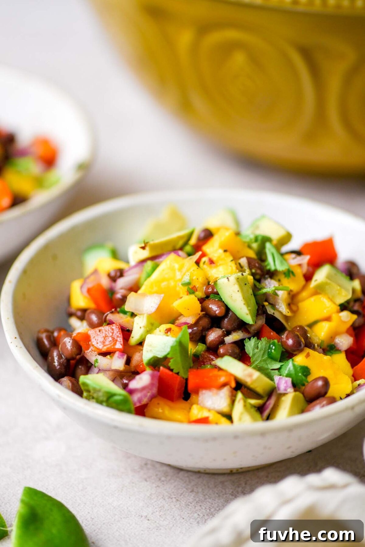 A close-up shot of a bowl of mango black bean salad, garnished with sliced avocado and fresh cilantro, highlighting its vibrant colors and appealing texture.