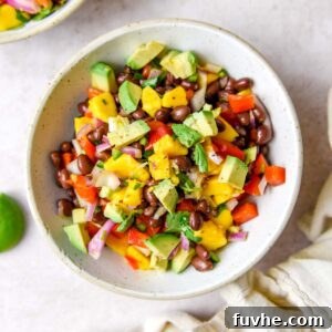 Bowl of mango and black bean salad with avocado, red bell pepper, red onion and cilantro.