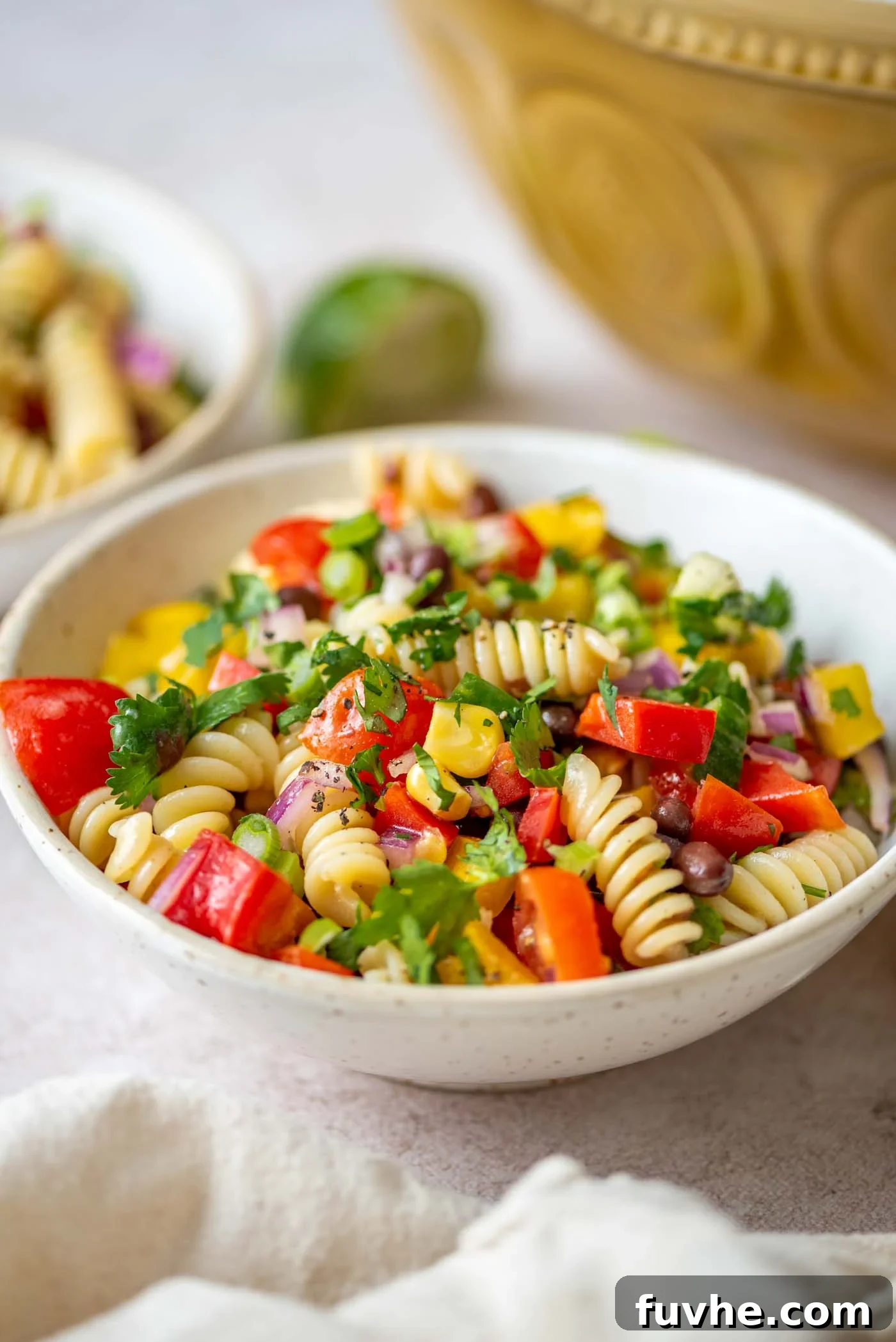 Vibrant vegan black bean pasta salad with fresh tomatoes, cucumber, cilantro, and corn, served in a large bowl, garnished with a lime wedge.