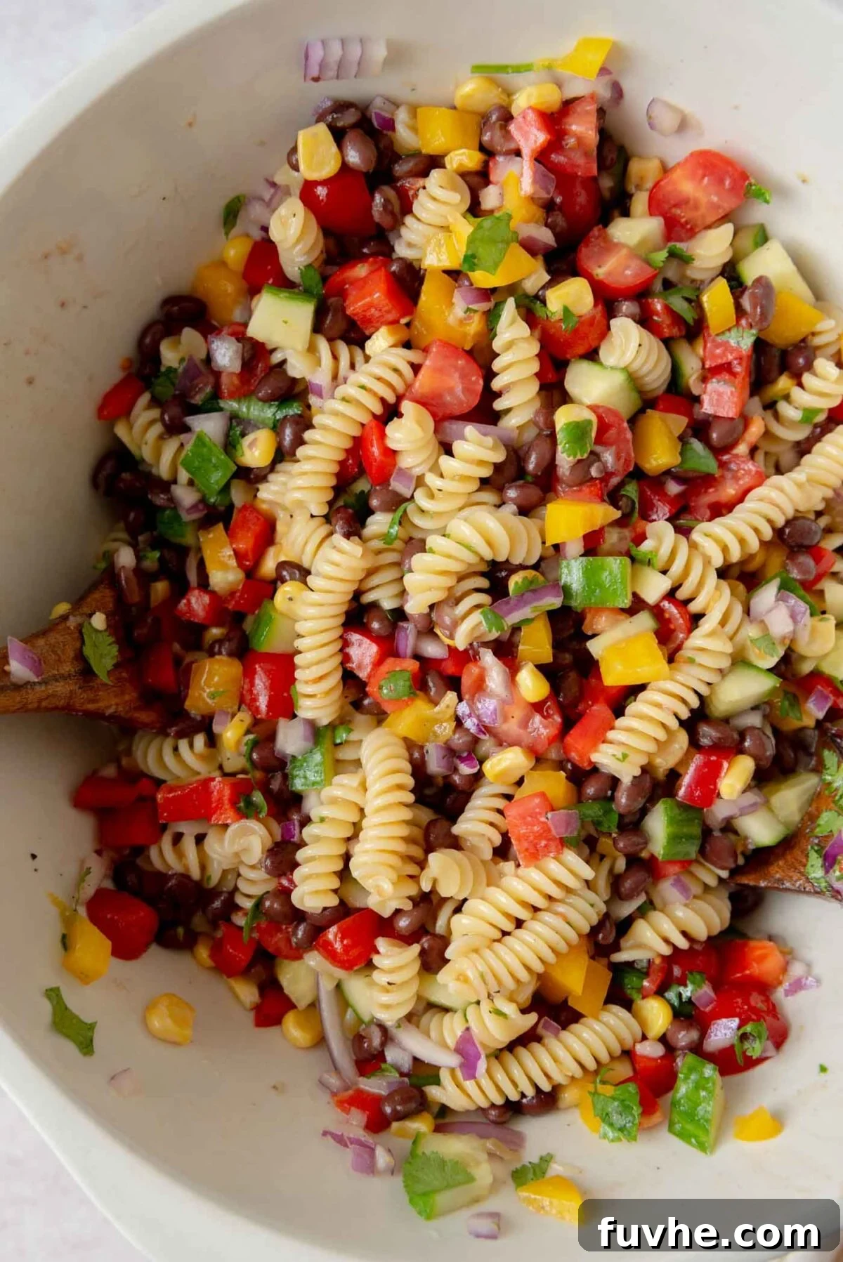 Large mixing bowl filled with a colorful black bean pasta salad, featuring corn, cucumber, and bell peppers, ready to be tossed.