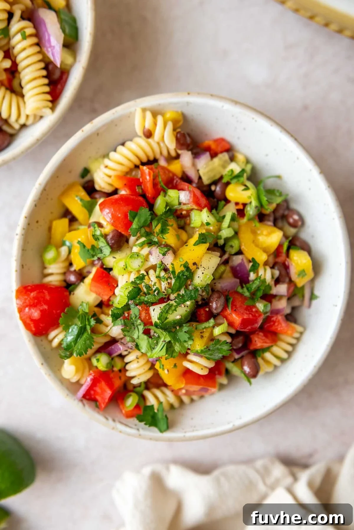A beautiful bowl of vegan black bean pasta salad, garnished with fresh cilantro and lime, showing vibrant colors of tomatoes, cucumber, and corn.