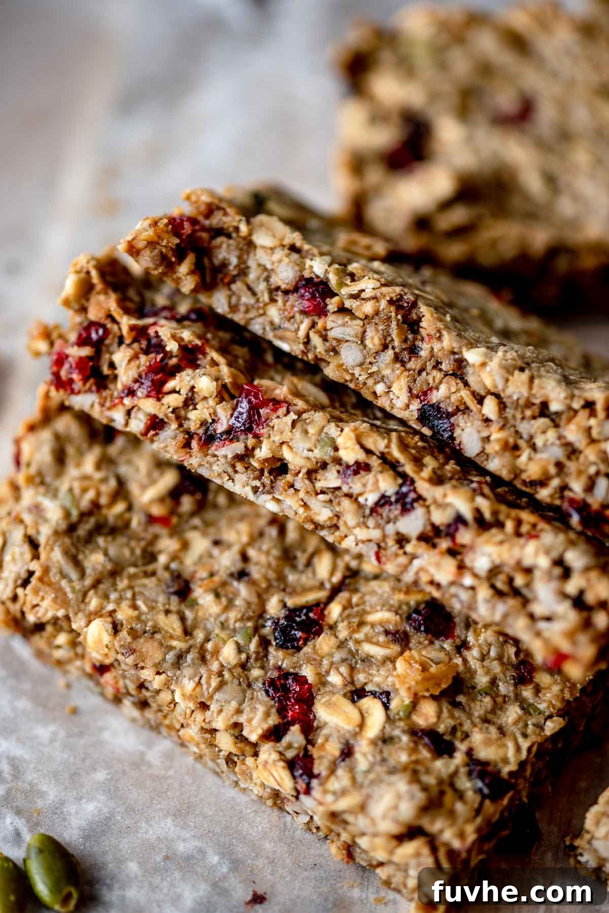 Wholesome Cranberry Granola Bars 8 Three perfectly golden-brown cranberry, sunflower seed, and pumpkin seed granola bars, artfully leaning against each other on a piece of parchment paper, highlighting their delicious texture and whole ingredients.