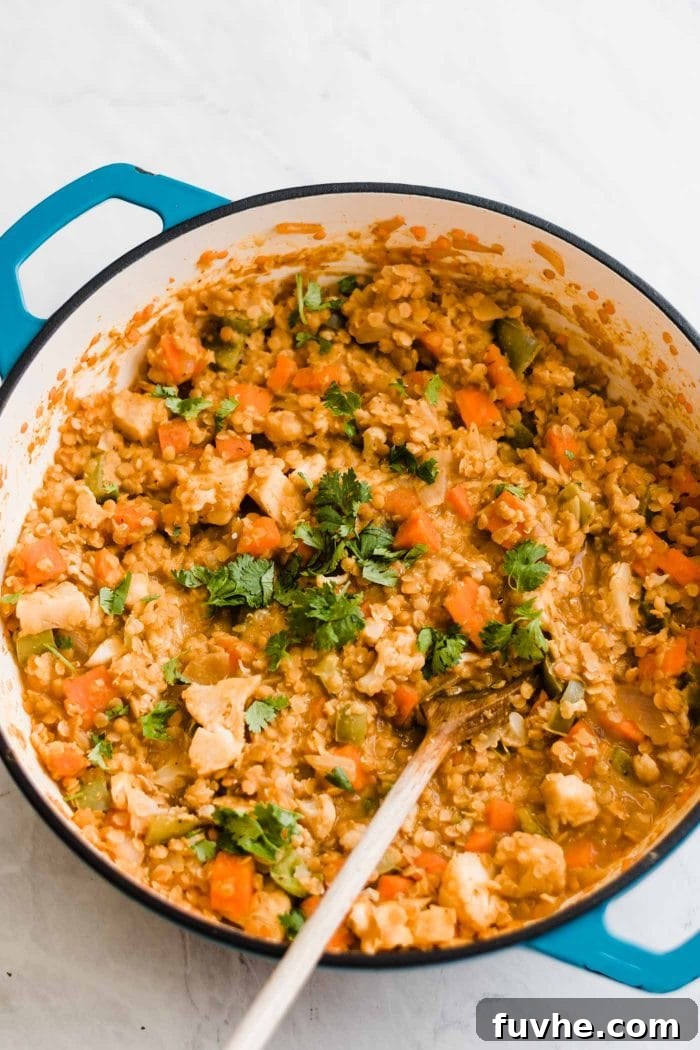 A finished red lentil curry dish with mixed vegetables, ready to serve in a large pot with a wooden spoon.