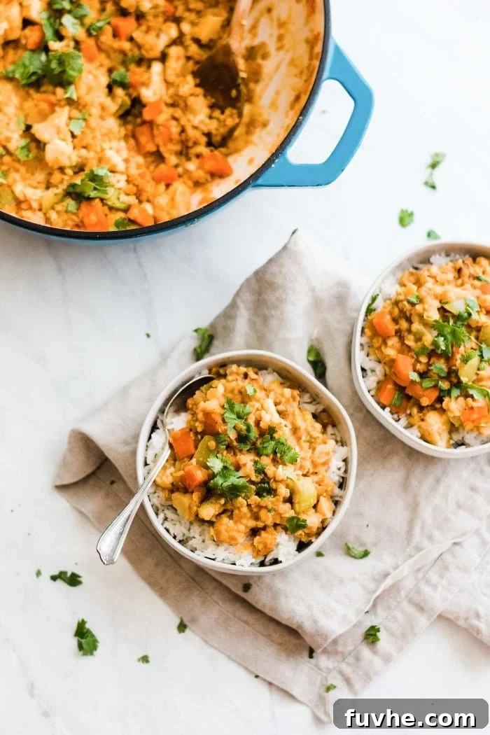 Two bowls of inviting red curry lentils with carrots and cauliflower, garnished with fresh herbs.