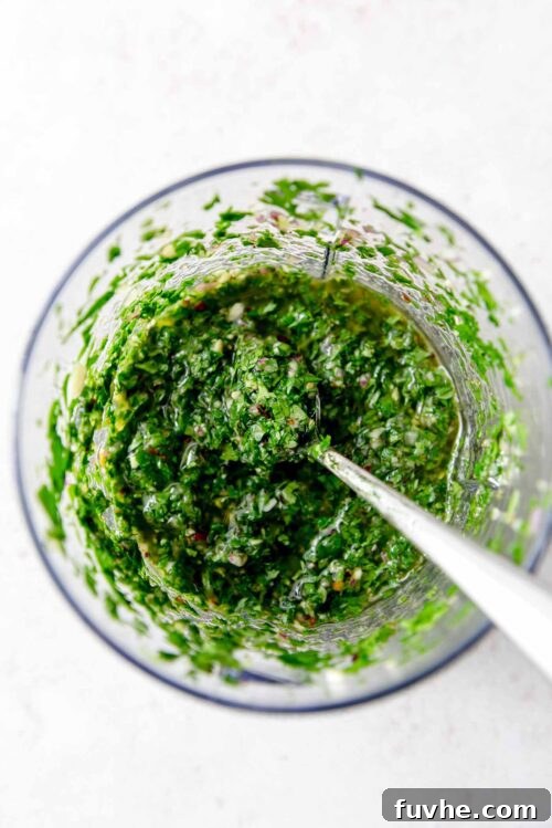Freshly blended chimichurri sauce in a food processor, with a spoon resting in it.
