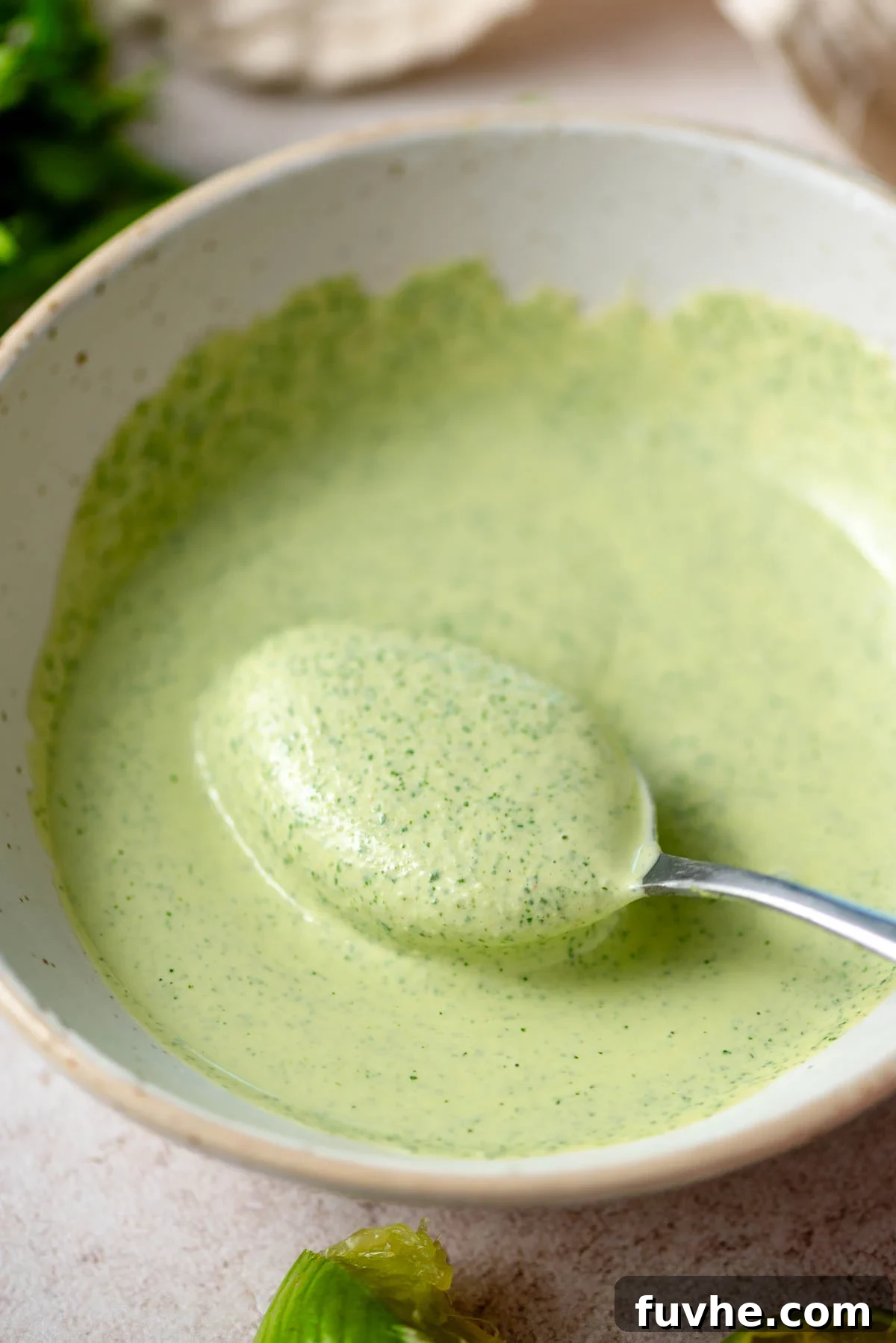 Spoon scooping creamy green tahini sauce in a bowl.