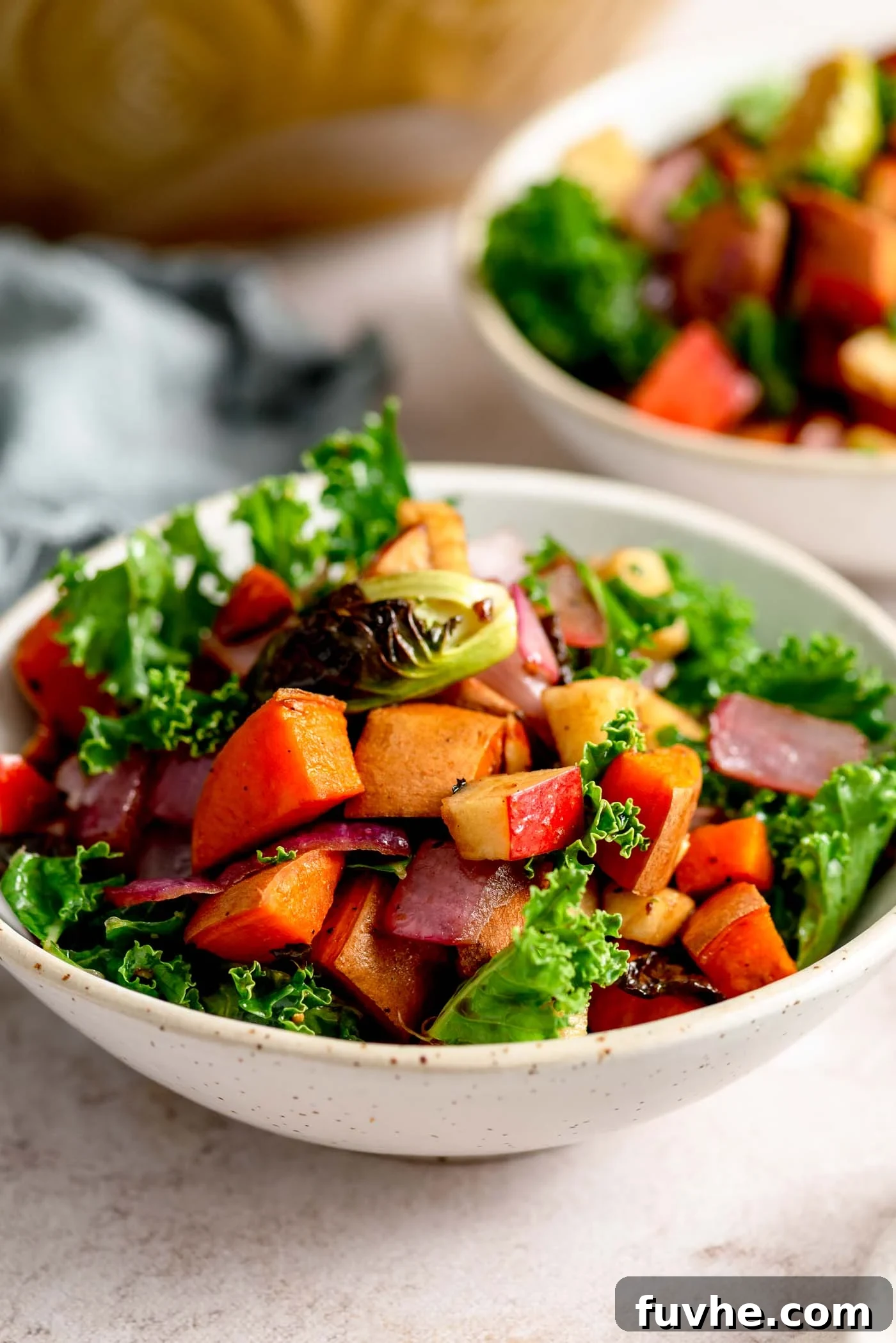 A beautifully presented roasted vegetable kale apple salad with sweet potato in an elegant small bowl, highlighting its vibrant colors and inviting texture.