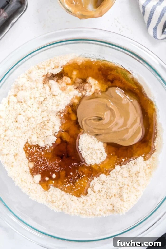 Almond flour and salt being mixed in a glass bowl, with sunflower seed butter and maple syrup waiting to be added.