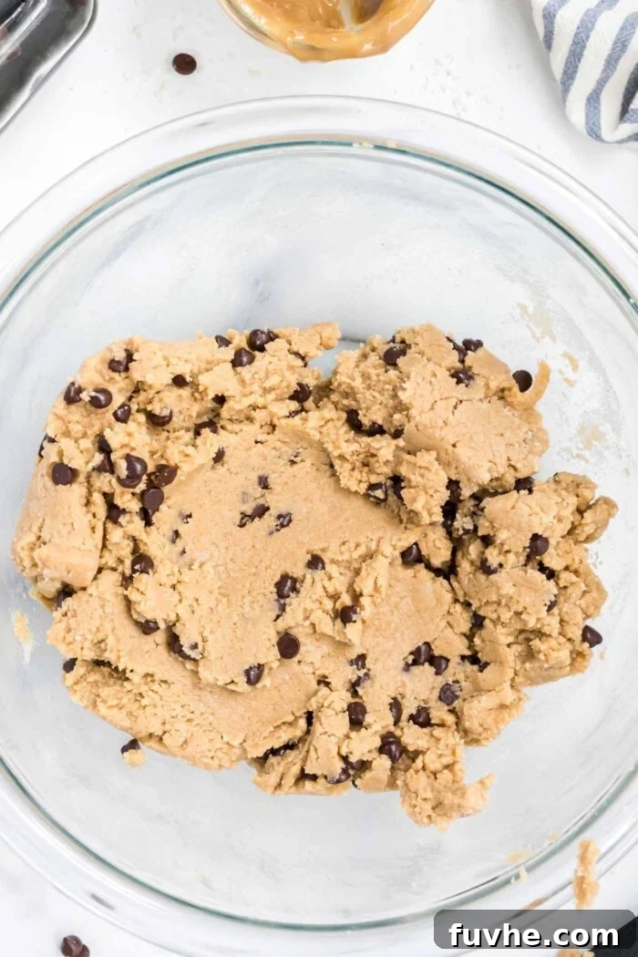 A glass mixing bowl filled with freshly made edible chocolate chip cookie dough, ready for scooping.