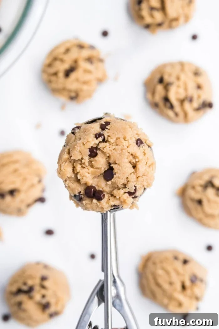 A small cookie scoop filled with perfect edible chocolate chip cookie dough, ready to be formed into a ball.