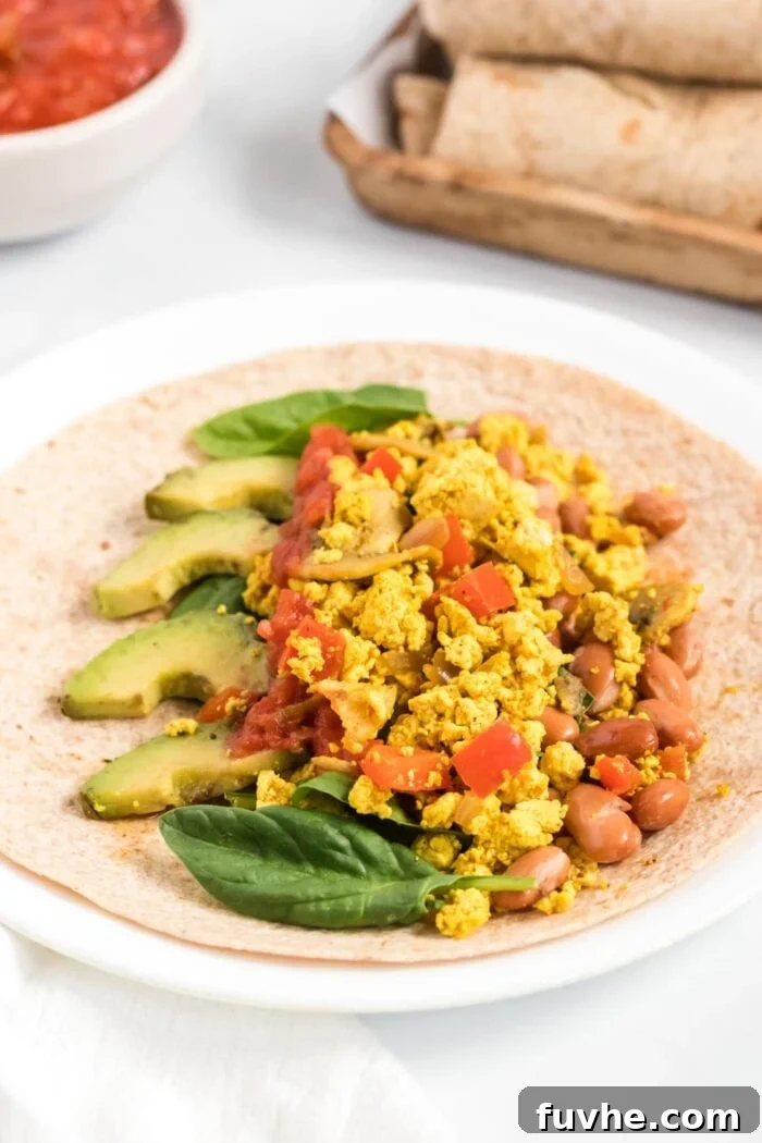 A tortilla laid flat with a generous amount of savory tofu scramble, creamy avocado slices, and hearty black beans neatly placed in the center, ready for rolling into a delicious breakfast burrito.