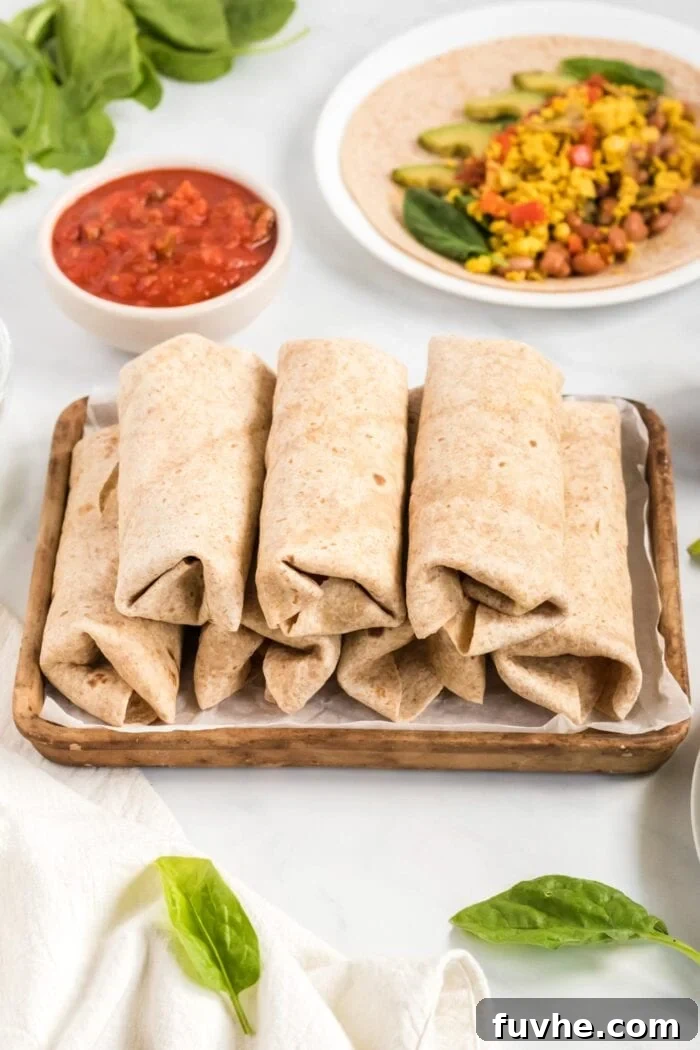 A pan filled with several freshly rolled vegan breakfast burritos, neatly arranged and ready to be served or prepared for storage. The burritos appear warm, golden, and perfectly sealed, showcasing a batch ready for enjoyment.