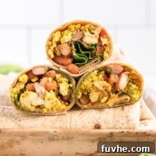 A close-up of a delicious vegan breakfast burrito, sliced in half to show its flavorful tofu scramble and other fillings.