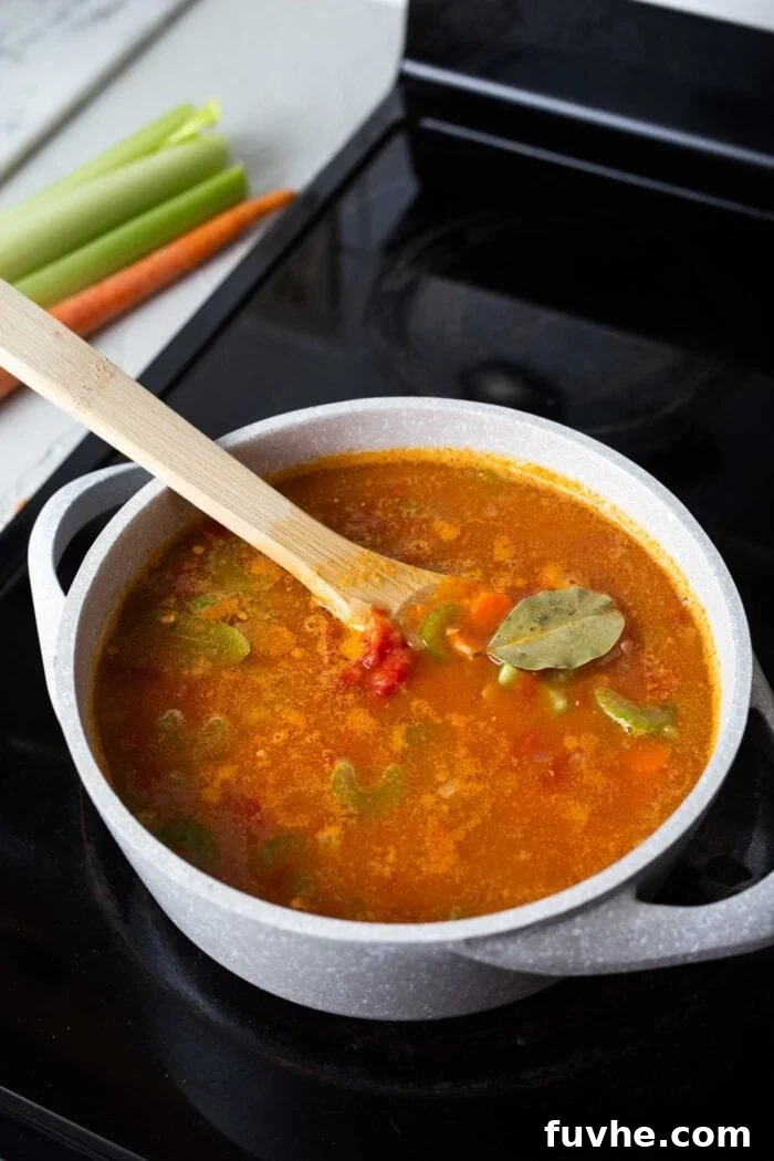 A large pot of rich red lentil tomato soup simmering gently on a stovetop burner, with a few bay leaves visible floating amidst the tender vegetables and lentils. The steam suggests it's perfectly cooked and ready to be served.