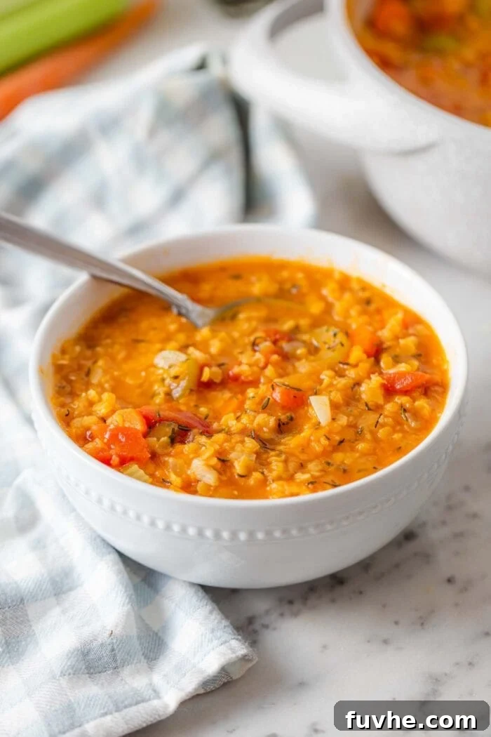 A beautifully presented bowl of red lentil tomato soup, garnished with fresh green herbs and a swirl of cream, placed on a light marble countertop, invitingly ready to be enjoyed.