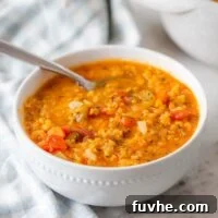 A bowl of rich red lentil tomato soup, beautifully garnished with fresh green herbs, resting on a clean marble countertop, ready for serving.
