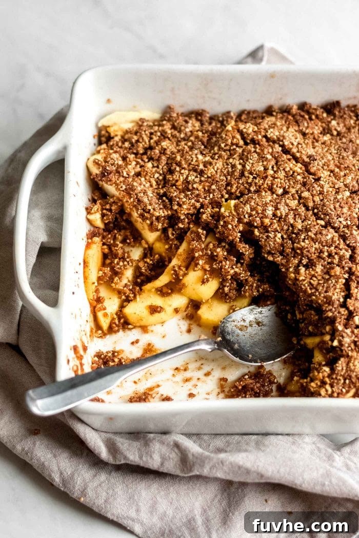 Grain-Free healthy vegan apple crisp in a white baking dish with a serving spoon.